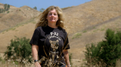 A woman with long, curly blonde hair stands in a black t-shirt that says "P-22."